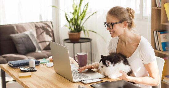 mulher sentada numa mesa em frente a um notebook, sorrindo com gato no colo