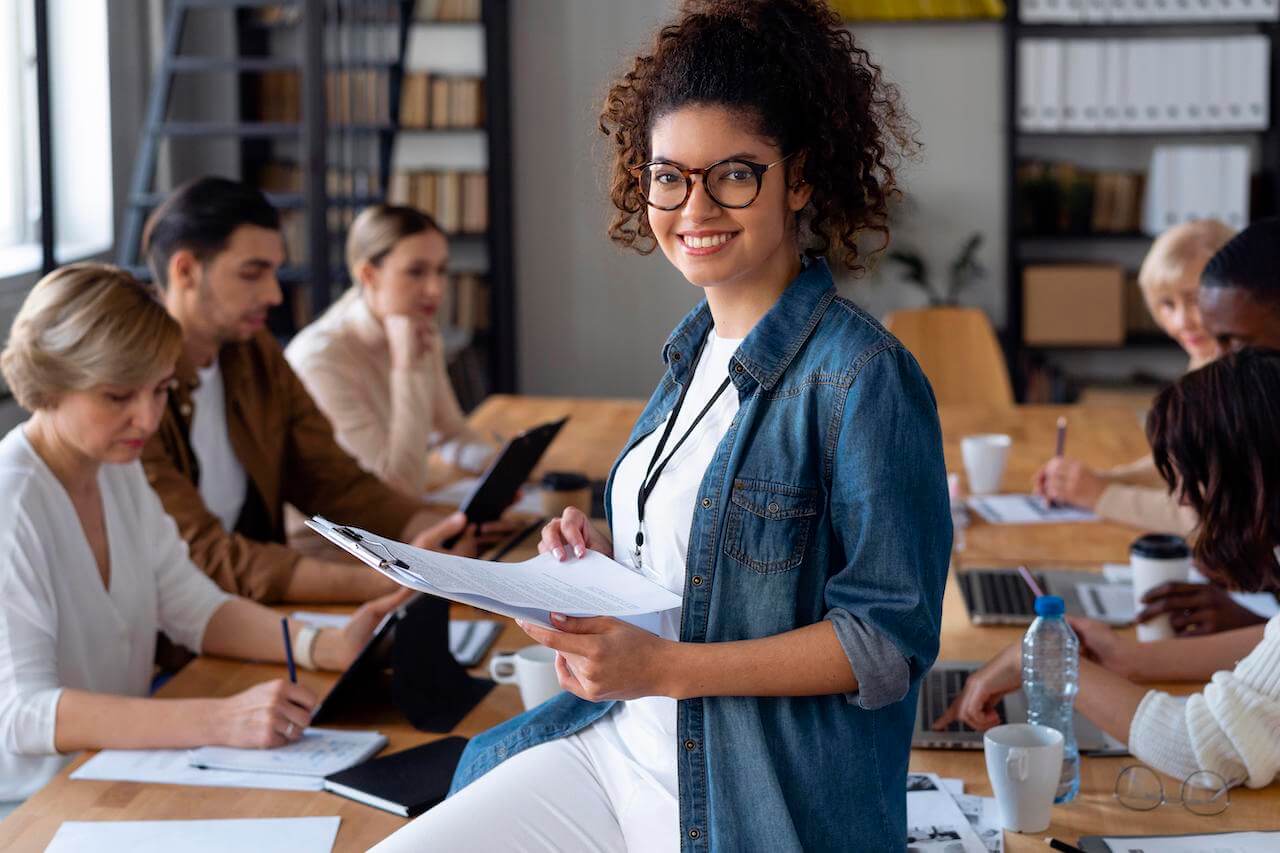 Anúncio perfeito: como destacar sua vaga e atrair melhores candidatos 1 mulher sorrindo em reunião com outras pessoas ao fundo